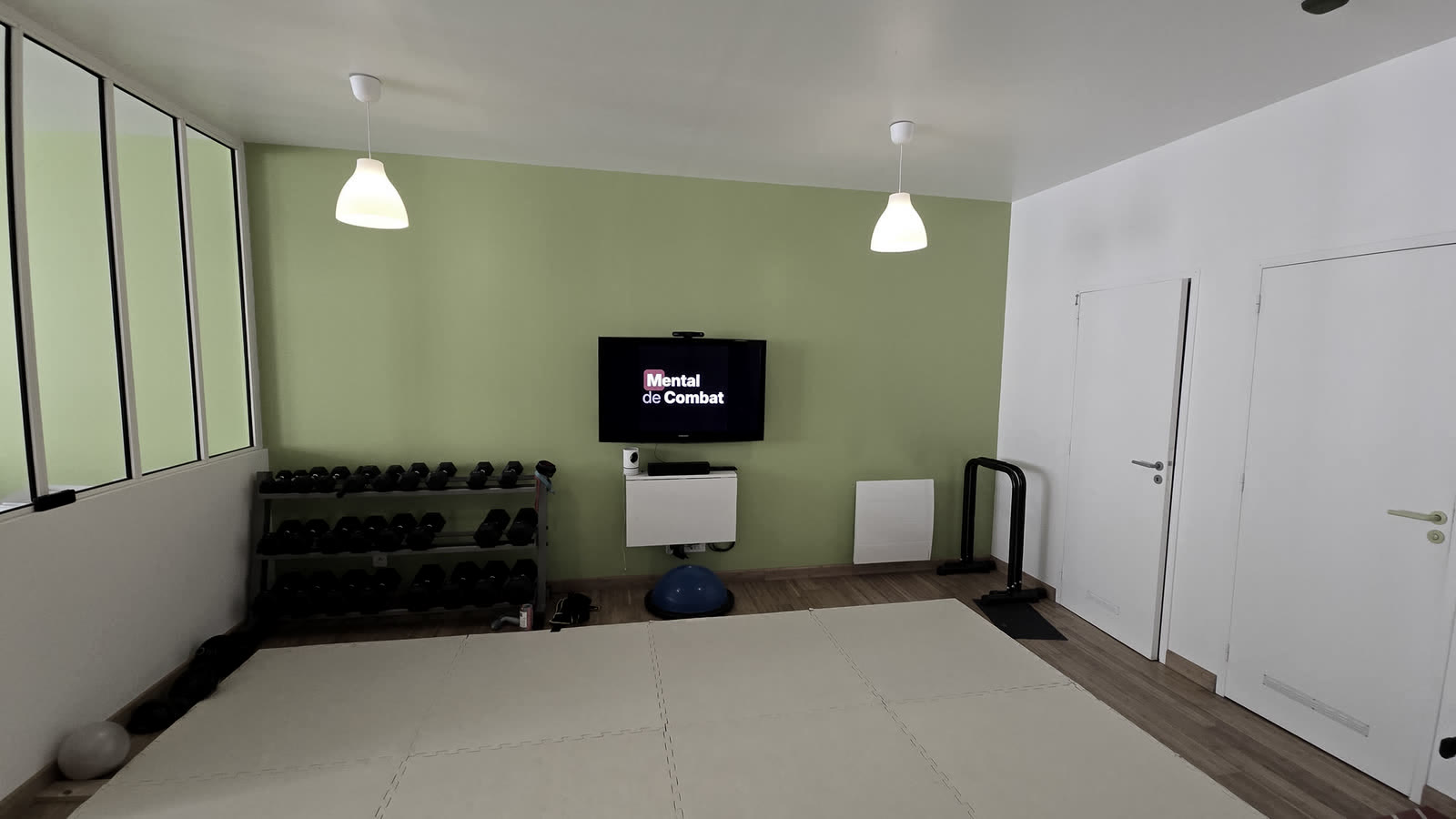 Salle équipée des locaux Mental de Combat à Bordeaux : tatamis, rack d'haltères et écran pour le travail physio